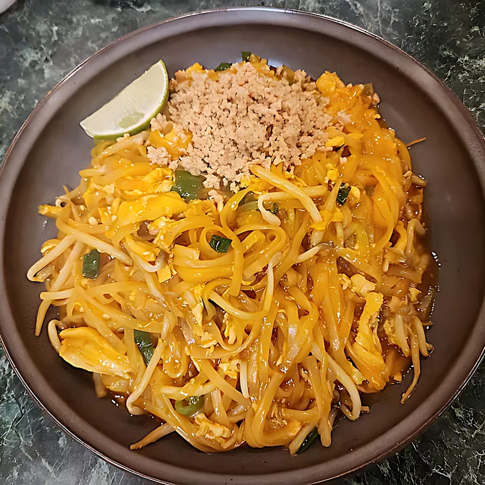A plate of Thai Cafe's Pad Thai noodles with scrambled egg, bean sprouts, crushed peanuts, and a lime wedge.