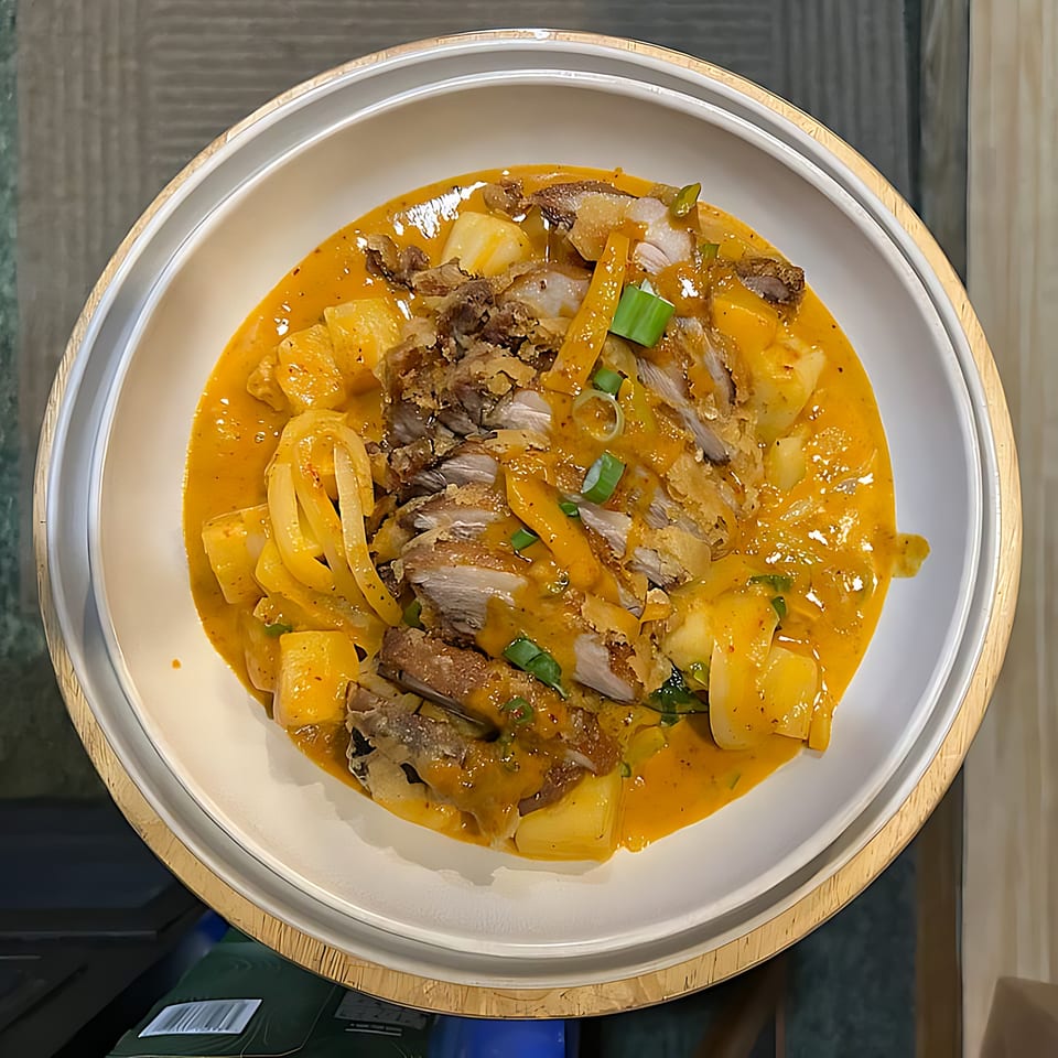 Close-up of Thai red curry with sliced duck, pineapple chunks, and green onions in a white bowl.