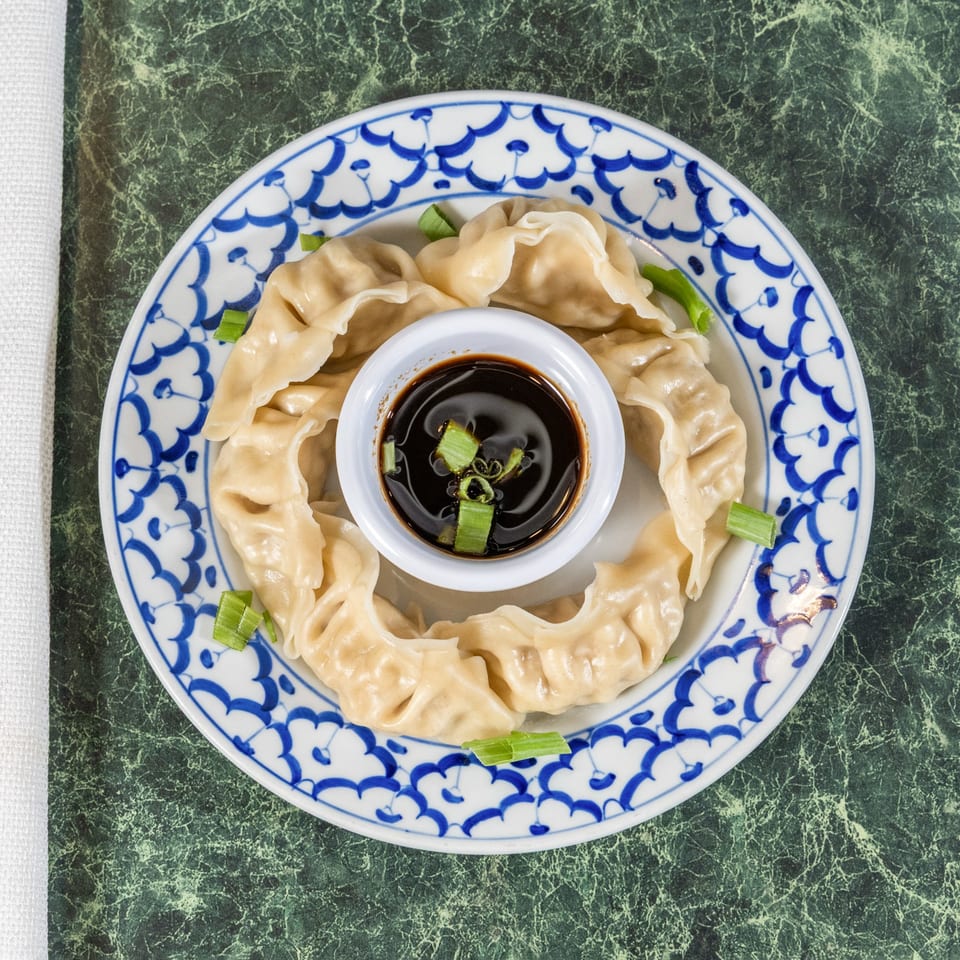 Steamed Thai dumplings arranged in a circle with a small bowl of soy sauce and scallions.