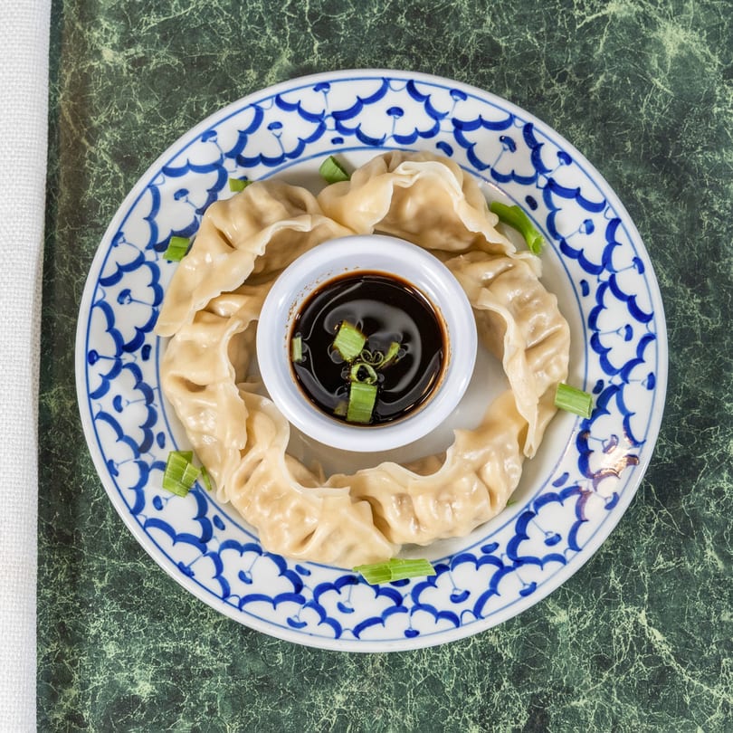 Steamed Thai dumplings arranged in a circle with a small bowl of soy sauce and scallions.