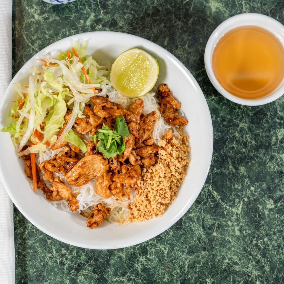 Thai Cafe's chicken vermicelli bowl with lettuce, carrots, lime, and a side of sauce.
