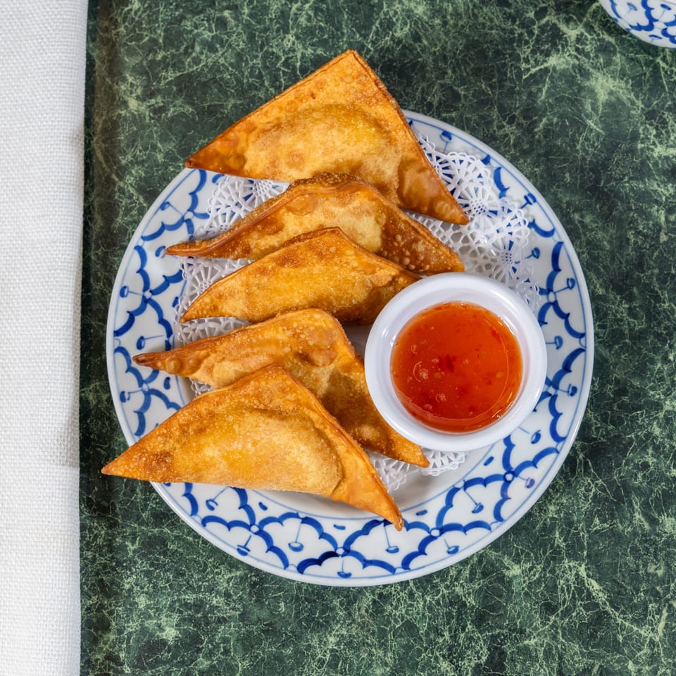 Golden-fried Thai Cafe crab rangoons with sweet chili dipping sauce on a blue and white plate.