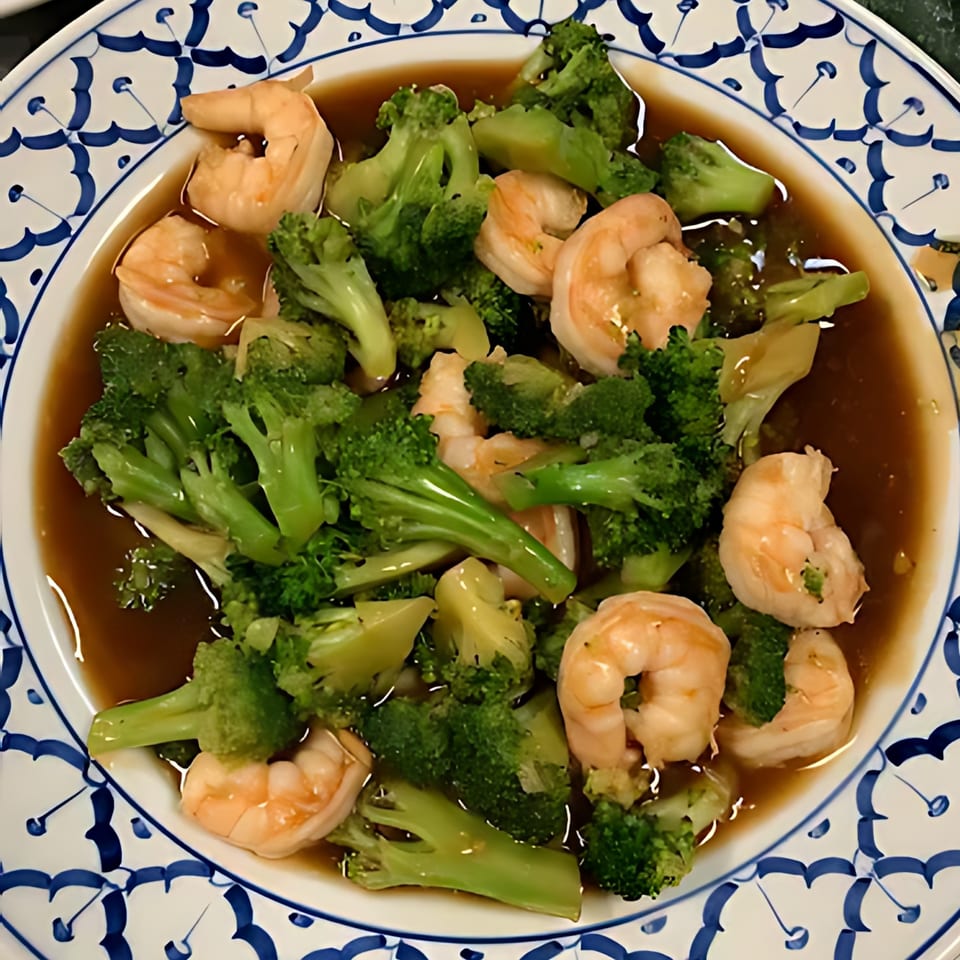 Shrimp and broccoli stir-fry in a savory brown sauce, served on a white and blue patterned plate.