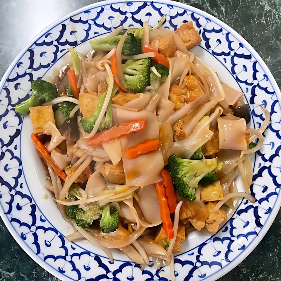 Thai Cafe's Pad See Ew with wide noodles, broccoli, carrots, and tofu on a blue and white plate.