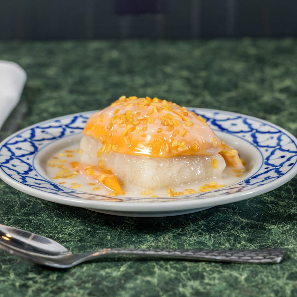 Thai Cafe's mango sticky rice dessert, topped with golden crispy mung beans, on a patterned plate.